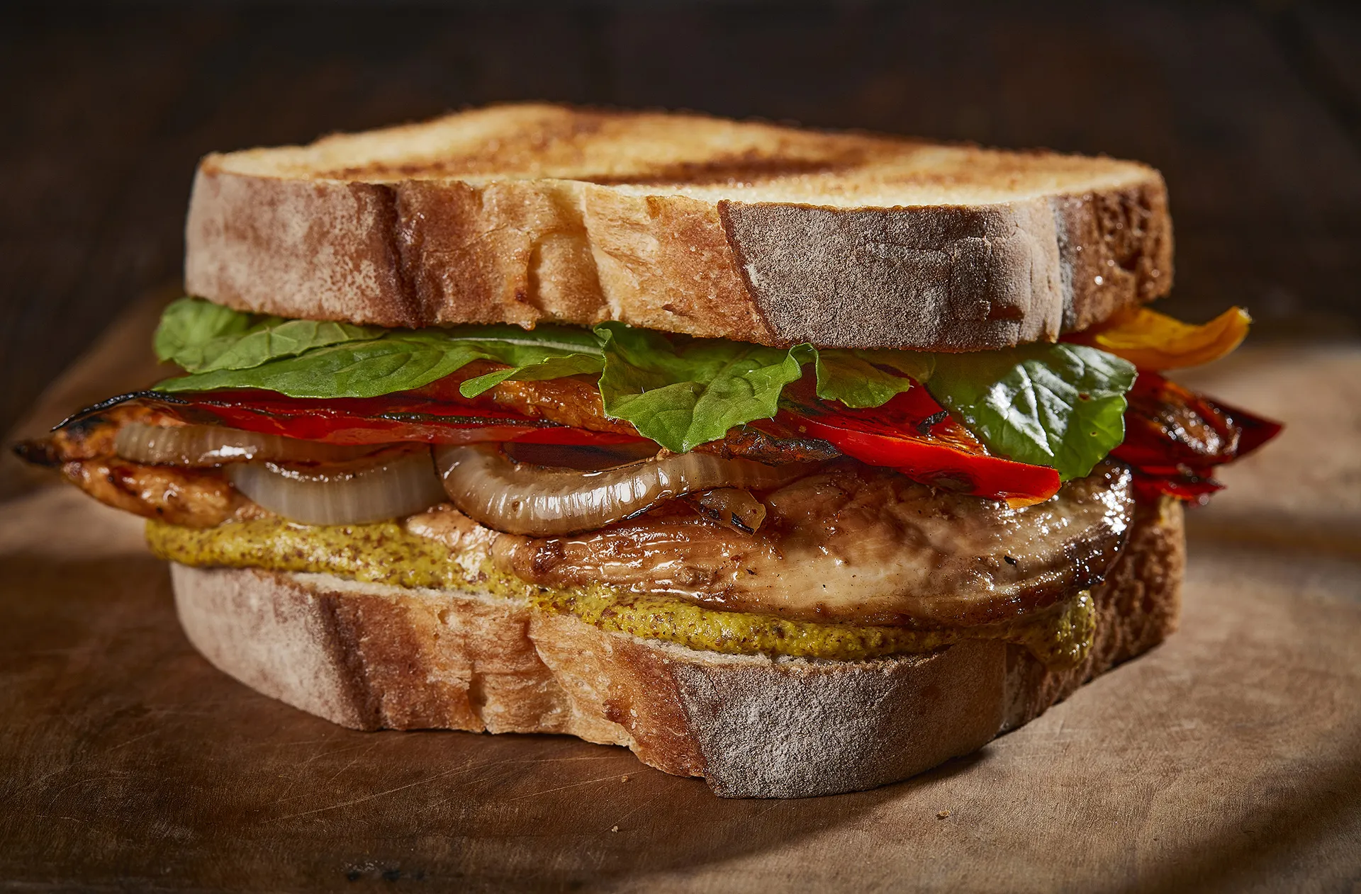 Sanduíche de frango com mostarda dijon, cebola caramelizada, pimentos e rúcula